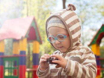 Ребенок в очках на детской площадке рассматривает игрушку